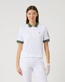 Woman wearing a white polo shirt with green accents and white pants on a light gray background