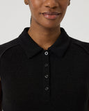 Woman wearing a black sleeveless dress with a collar against a plain background