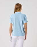 Woman wearing a light blue polo shirt and white pants on a plain background