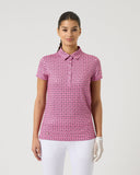 Woman wearing a pink patterned polo shirt and white pants on a light gray background