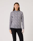 Woman wearing a patterned long-sleeve shirt and black pants on a light gray background