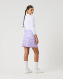 Person wearing a white long-sleeve top and patterned skirt on a plain background