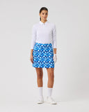 Woman wearing a white golf shirt, blue floral skirt, and white shoes on a light gray background