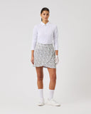 Woman wearing a white shirt and patterned skirt on a plain background