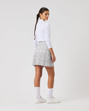 Person wearing a white long-sleeve shirt and patterned skirt on a plain background