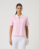 Woman wearing a pink polo shirt and white pants on a light gray background