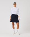 Woman wearing a white polo shirt, navy skirt, and white shoes on a white background