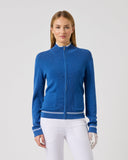 Woman wearing a blue jacket and white pants on a gray background