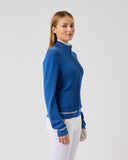 Woman wearing a blue jacket and white pants on a light gray background