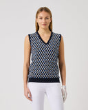 Woman wearing a sleeveless patterned top and white pants on a plain background