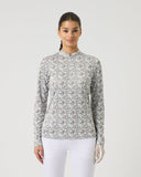 Woman wearing a patterned long-sleeve top and white pants on a light gray background