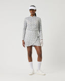 Person wearing a patterned dress, visor, and white shoes on a plain background