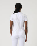 Person wearing a white polo shirt with black patterns on a plain background