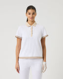 Woman wearing a white polo shirt with beige accents and white pants on a light gray background