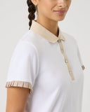 Woman wearing a white polo shirt with beige accents on a plain background