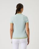 Woman wearing a light green checkered shirt and white pants on a plain background