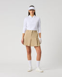 A woman modeling a white long-sleeve polo shirt, beige pleated tennis skirt, white visor, white gloves, white socks, and white sneakers against a light gray studio background.