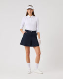 Woman in golf attire with a white shirt, navy skirt, and visor on a light gray background