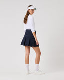 Woman wearing a white long-sleeve top, navy skirt, and visor on a white background