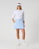Daily Sports Woven Light Blue Skort in powder blue – women's A-line woven golf skort with structured waistband, silver logo button and side zip pocket, full length front view on model styled with white 3/4 sleeve polo, white visor and golf glove