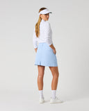 Daily Sports Woven Light Blue Skort in powder blue – women's A-line woven golf skort showing back kick pleat, structured waistband and clean tailored fit, three-quarter back view on model styled with white 3/4 sleeve polo and white visor