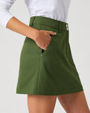 Daily Sports Woven Khakora Skort close-up of green woven fabric with structured waistband, silver logo button, angled side pocket and zip security pocket detail, side view