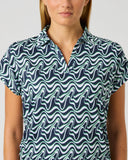 A woman wearing a short-sleeve collared button-up shirt with a navy blue and mint green wavy abstract pattern, shown against a plain light gray background.