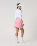 A woman stands in profile wearing a white long-sleeve top, a pink and white gingham mini skirt, white socks, and white sneakers against a light gray studio background.