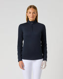 A woman modeling a dark navy long-sleeve quarter-zip performance top with white riding breeches, standing against a light gray studio background.