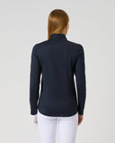 A woman viewed from the back wearing a dark navy long-sleeve mock-neck athletic top and white pants, standing against a light gray studio background.