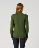 A woman viewed from the back wearing an olive green long-sleeve mock neck top and dark navy pants, standing against a light gray studio background.