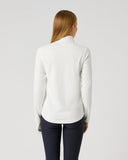 A woman viewed from behind wearing a white long-sleeve mock-neck top and dark navy pants, standing against a plain light gray studio background.