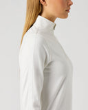 A woman shown in side profile wearing a fitted white mock-neck or high-neck long-sleeve top against a plain light gray studio background.