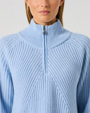 Close-up of women's light blue ribbed wool blend golf pullover with half zip, high collar, and Daily Sports branded silver zipper pull
