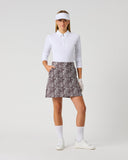 Daily Sports Dull Zebra Printed Skort in muted brown and white abstract zebra swirl print – women's A-line golf skort with side pockets and elasticated waistband, full length front view on model styled with white long sleeve polo and viso