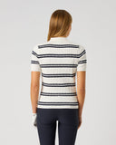 A woman viewed from the back wearing a short-sleeve ribbed knit polo shirt with horizontal navy and white stripes, paired with dark navy pants, against a light gray studio background.
