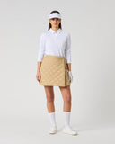 Women's camel quilted golf skirt with diamond pattern and wrap-style front – front view styled with white golf top and visor
