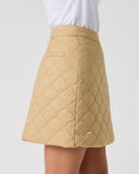 Close-up of women's camel quilted golf skirt showing diamond quilt pattern, side pocket, and Daily Sports logo tab
