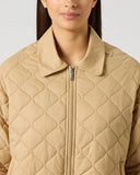 Close-up of women's camel quilted golf jacket with diamond and wave quilt pattern, polo collar, and silver full-length zipper
