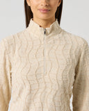 Close-up of women's cream desert structure long sleeve golf top with wave texture fabric, half zip, and stand-up collar detail
