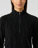Close-up of women's black structure long sleeve golf top with wave texture fabric, half zip, and silver zipper pull detail

