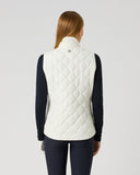 A woman viewed from the back wearing a white quilted sleeveless vest over a dark navy long-sleeve top and navy leggings, against a plain light gray studio background.