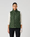 A model wearing a dark green diamond-quilted zip-up puffer vest over a white long-sleeve top and black pants, standing against a light gray studio background.