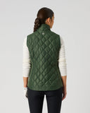 A woman viewed from the back wearing a dark green diamond-quilted sleeveless puffer vest over a white long-sleeve top and black pants, standing against a light gray studio background.