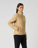 A woman modeling a beige quilted zip-up jacket with a high stand-up collar, paired with black pants, against a plain light gray studio background.