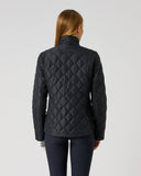 A woman viewed from the back wearing a black quilted jacket and dark pants against a plain light gray studio background.