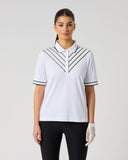 A woman modeling a white short-sleeve polo shirt with black striped chevron detailing on the chest and collar, paired with black pants, against a light gray studio background.