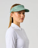 A woman in a white polo shirt wearing a green and white patterned visor, shown in profile against a light gray studio background.