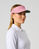 A woman in a white collared polo shirt wearing a red and white patterned visor, photographed against a solid light gray background.