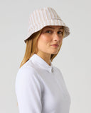 A woman wearing a white long-sleeve collared shirt and a beige bucket hat with thin vertical white stripes, photographed against a light gray studio background.